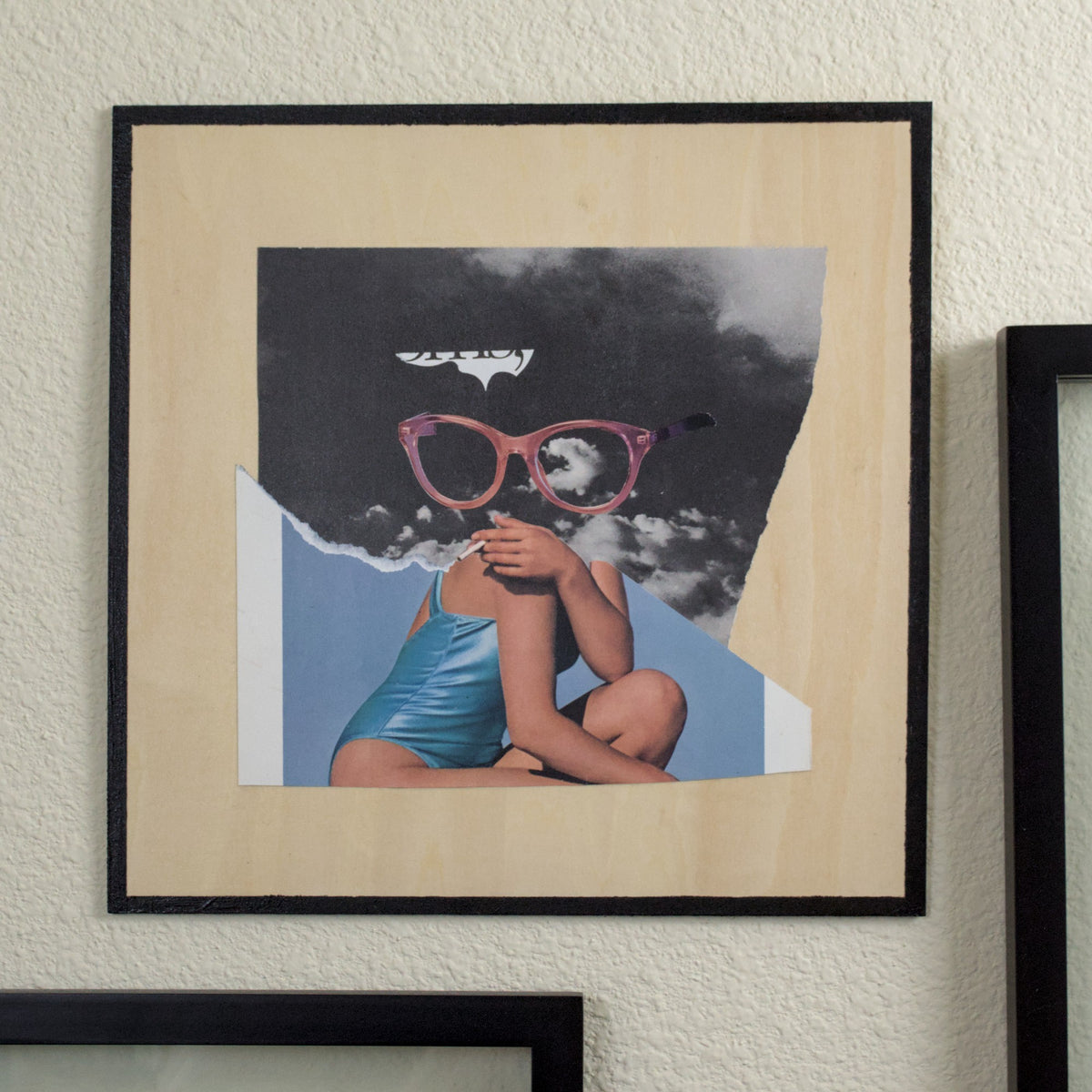 A collage on a wooden panel with a quarter-inch black border. A woman in a teal one-piece swimsuit leans casually on her knee with a cigarette. Her head has been replaced with a large pair of chic pink glasses, which float against a black and white photo of stormy clouds. An abstract sliver with the edge of some text points toward the glasses above the brow on the left side, like an esoteric speech bubble. The lower page has been torn so that the edge forms a line of smoke trailing from the cigarette.